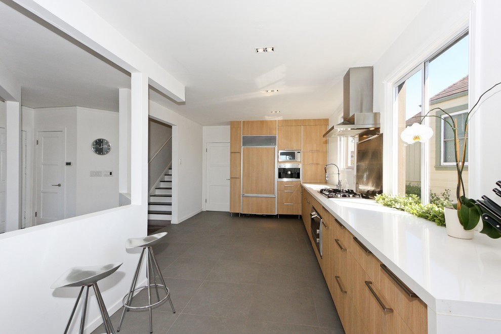 На фото: угловая кухня в современном стиле с плоскими фасадами, светлыми деревянными фасадами, техникой под мебельный фасад и окном с