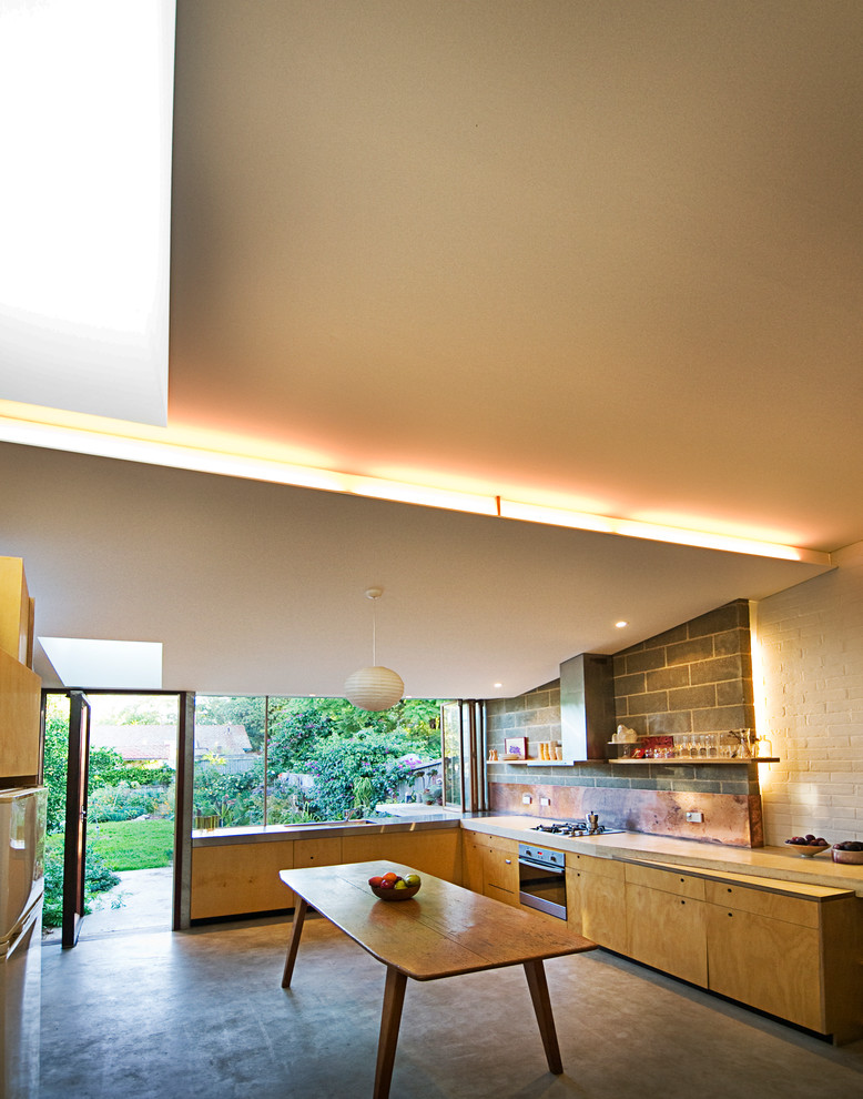 На фото: угловая кухня среднего размера в стиле ретро с плоскими фасадами, фартуком цвета металлик, врезной мойкой, фасадами цвета дерева среднего тона, столешницей из бетона и бетонным полом