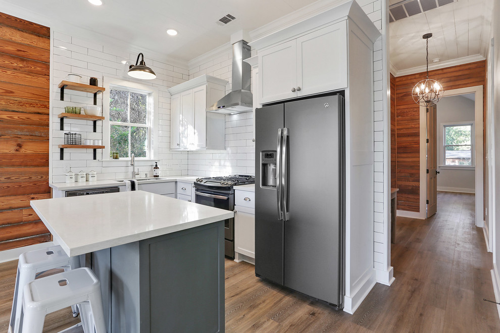 Exemple d'une petite cuisine américaine chic en L avec un évier encastré, un placard à porte shaker, des portes de placard blanches, un plan de travail en quartz modifié, une crédence blanche, une crédence en carrelage métro, un électroménager en acier inoxydable, un sol en vinyl et îlot.