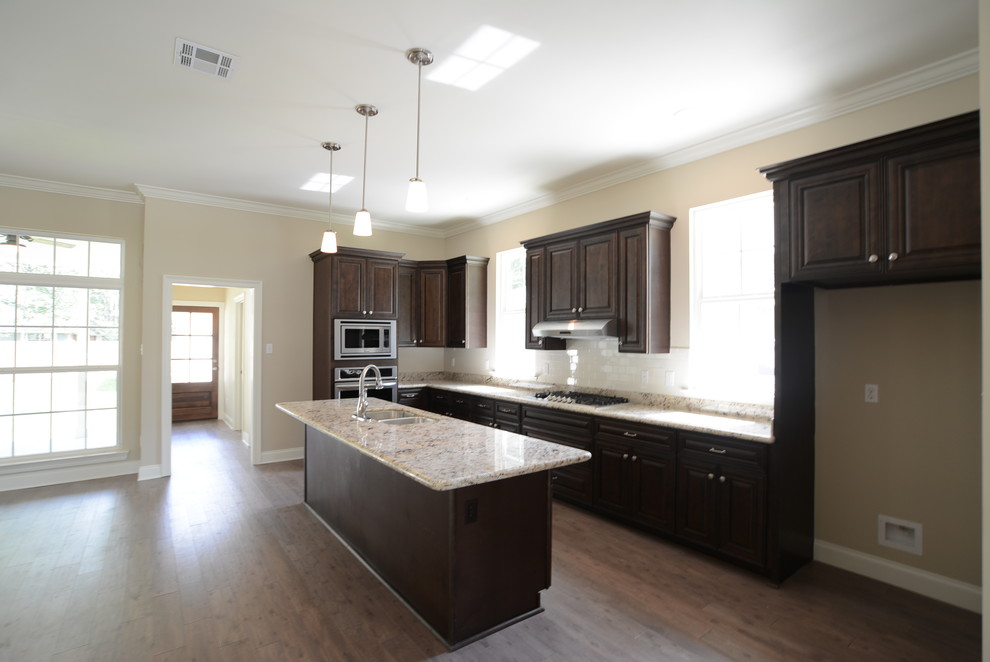 Inspiration for a mid-sized craftsman l-shaped medium tone wood floor open concept kitchen remodel in New Orleans with a double-bowl sink, raised-panel cabinets, dark wood cabinets, granite countertops, white backsplash, subway tile backsplash, stainless steel appliances and an island