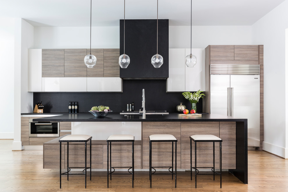 Contemporary galley kitchen in Houston with flat-panel cabinets, medium wood cabinets, black splashback, stainless steel appliances, medium hardwood flooring, an island, brown floors and black worktops.