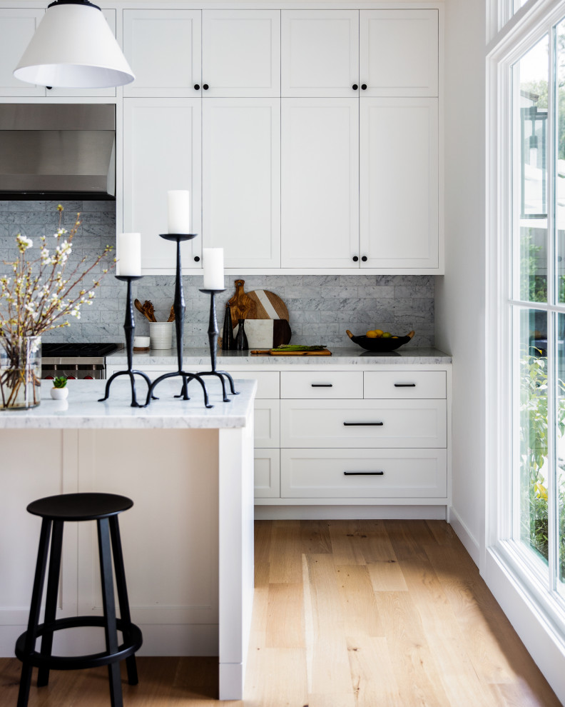 Large classic galley kitchen in San Francisco with shaker cabinets, white cabinets, grey splashback, stainless steel appliances, light hardwood flooring, an island, beige floors and grey worktops.
