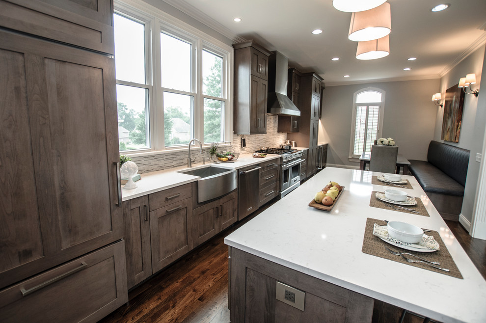 Large traditional galley kitchen/diner in Nashville with a belfast sink, shaker cabinets, grey cabinets, engineered stone countertops, white splashback, stone tiled splashback, stainless steel appliances, dark hardwood flooring and an island.