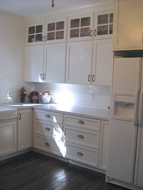 Bild på ett mellanstort lantligt kök, med en rustik diskho, luckor med infälld panel, vita skåp, marmorbänkskiva, vitt stänkskydd, stänkskydd i tunnelbanekakel, vita vitvaror och mörkt trägolv