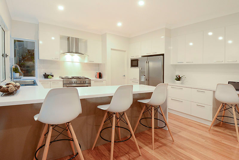 Inspiration for a medium sized contemporary u-shaped open plan kitchen in Brisbane with a double-bowl sink, flat-panel cabinets, white cabinets, white splashback, glass sheet splashback, stainless steel appliances, light hardwood flooring, a breakfast bar, wood worktops and white worktops.