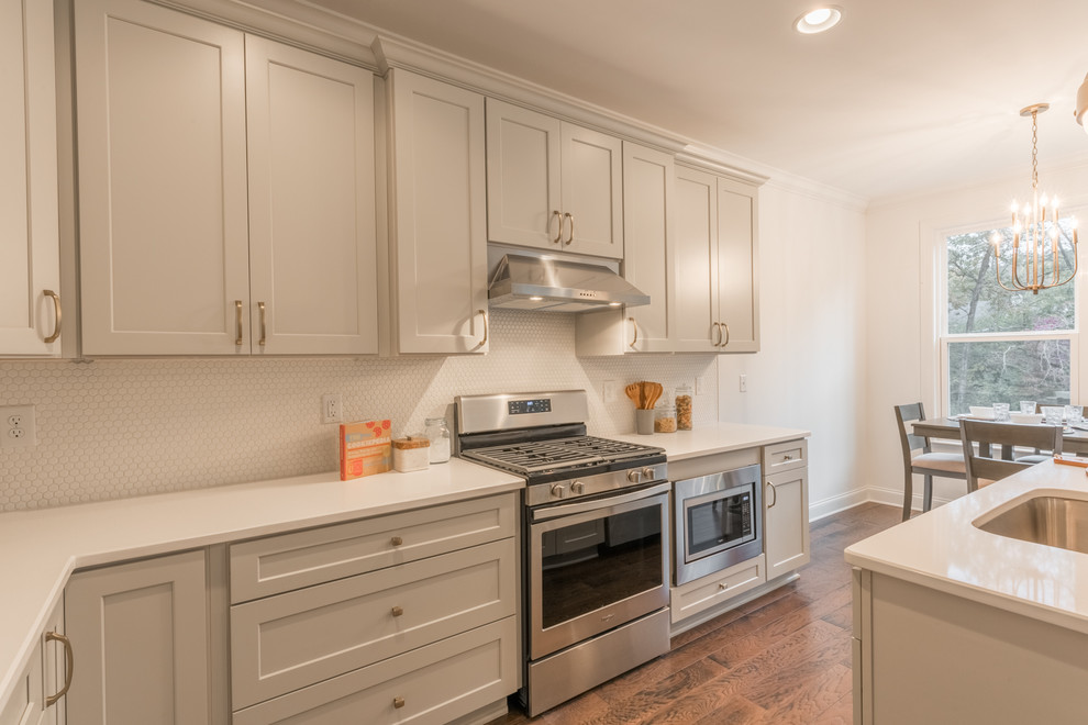 Foto på ett mellanstort amerikanskt vit kök, med en undermonterad diskho, skåp i shakerstil, grå skåp, bänkskiva i koppar, vitt stänkskydd, stänkskydd i mosaik, rostfria vitvaror, mellanmörkt trägolv, en köksö och brunt golv