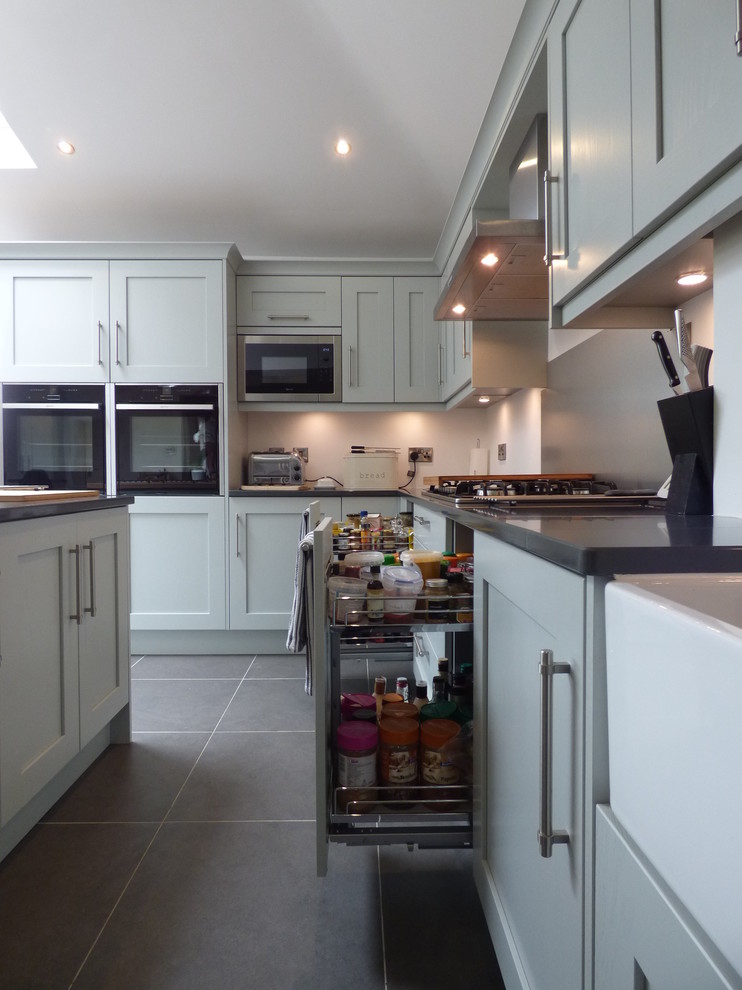 Large eclectic u-shaped kitchen/diner in Other with a belfast sink, shaker cabinets, grey cabinets, quartz worktops, metallic splashback, black appliances and an island.