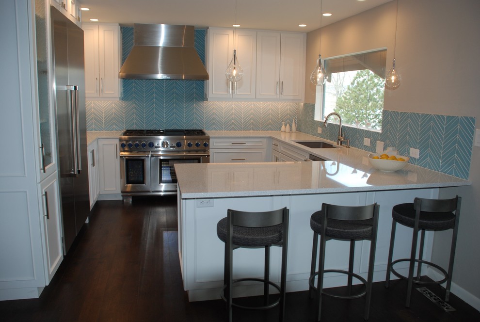 Bild på ett litet maritimt vit vitt kök, med en undermonterad diskho, vita skåp, bänkskiva i kvarts, blått stänkskydd, stänkskydd i glaskakel, rostfria vitvaror, mörkt trägolv, en halv köksö och brunt golv