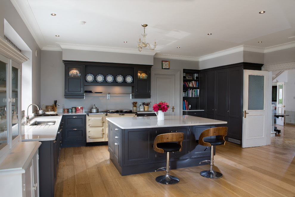 Mittelgroße Klassische Wohnküche in L-Form mit Schrankfronten mit vertiefter Füllung, Quarzit-Arbeitsplatte, hellem Holzboden und Kücheninsel in Cork
