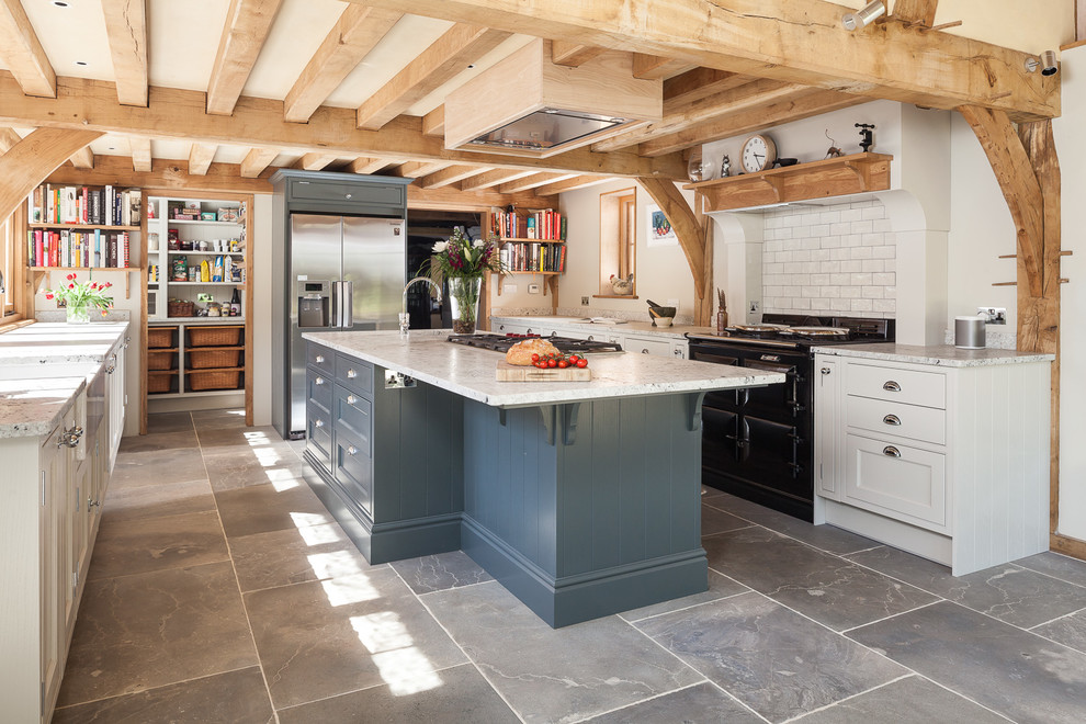 Elegant gray floor kitchen photo in Kent with a farmhouse sink, white cabinets, white backsplash, subway tile backsplash, black appliances and an island