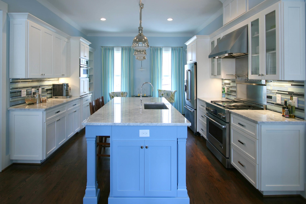 Inredning av ett klassiskt kök och matrum, med en undermonterad diskho, släta luckor, vita skåp, marmorbänkskiva, blått stänkskydd, stänkskydd i glaskakel, rostfria vitvaror, mörkt trägolv och en köksö