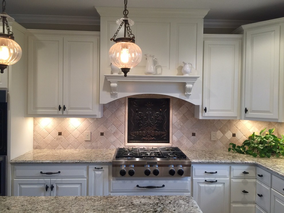 Lantlig inredning av ett kök, med granitbänkskiva, beige stänkskydd, stänkskydd i stenkakel och rostfria vitvaror