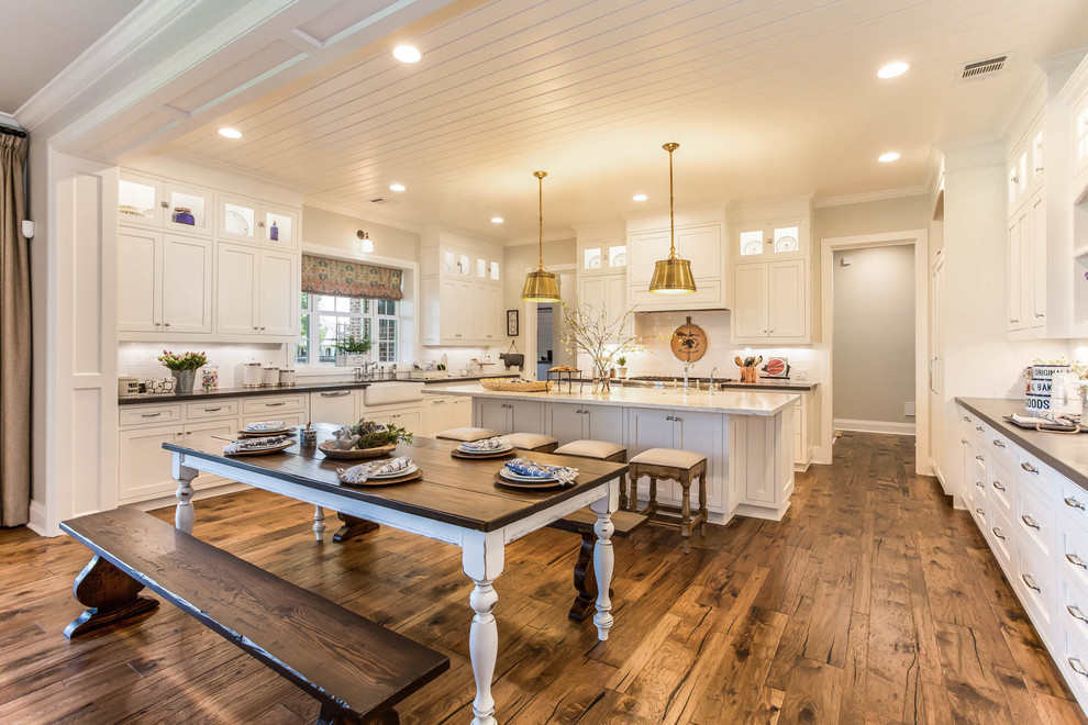 Landhaus Küche mit Landhausspüle, weißen Schränken, Küchenrückwand in Weiß, braunem Holzboden, Kücheninsel und braunem Boden in Houston