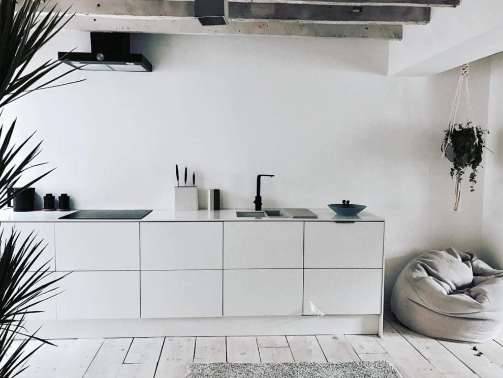This is an example of a medium sized scandinavian galley open plan kitchen in London with a built-in sink, flat-panel cabinets, white cabinets, engineered stone countertops, black appliances, painted wood flooring and no island.