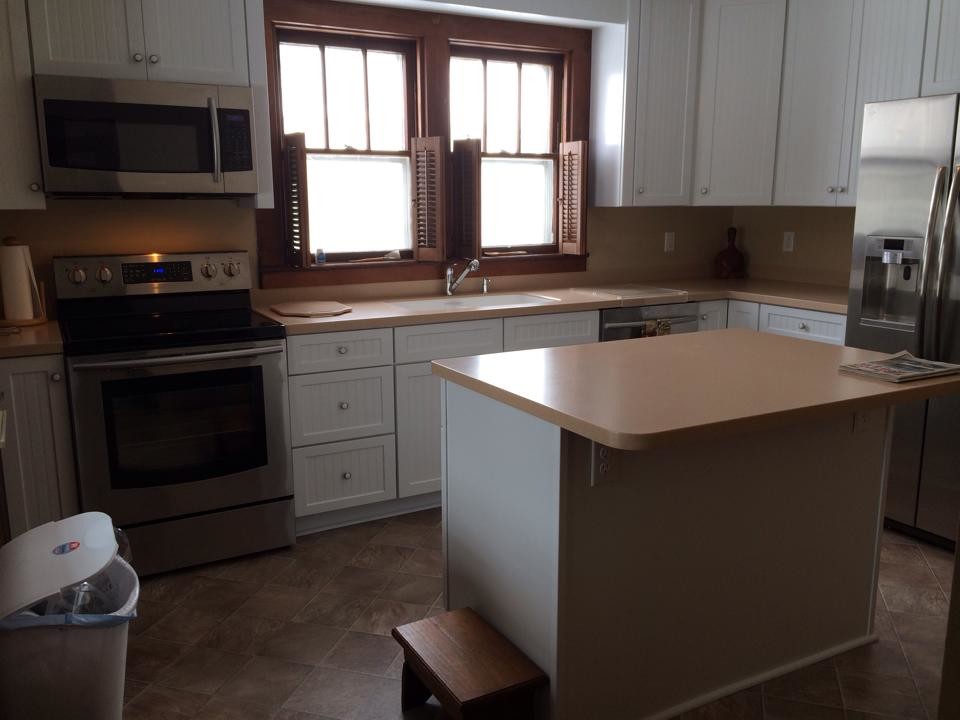 Example of a mid-sized l-shaped vinyl floor kitchen design in Other with an island, recessed-panel cabinets, white cabinets, solid surface countertops, stainless steel appliances and an integrated sink