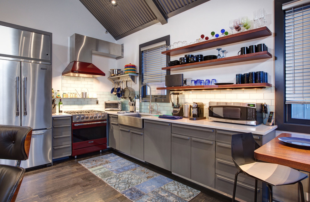 На фото: угловая кухня-гостиная в современном стиле с фартуком из плитки кабанчик, с полувстраиваемой мойкой (с передним бортиком), плоскими фасадами, серыми фасадами, белым фартуком и цветной техникой