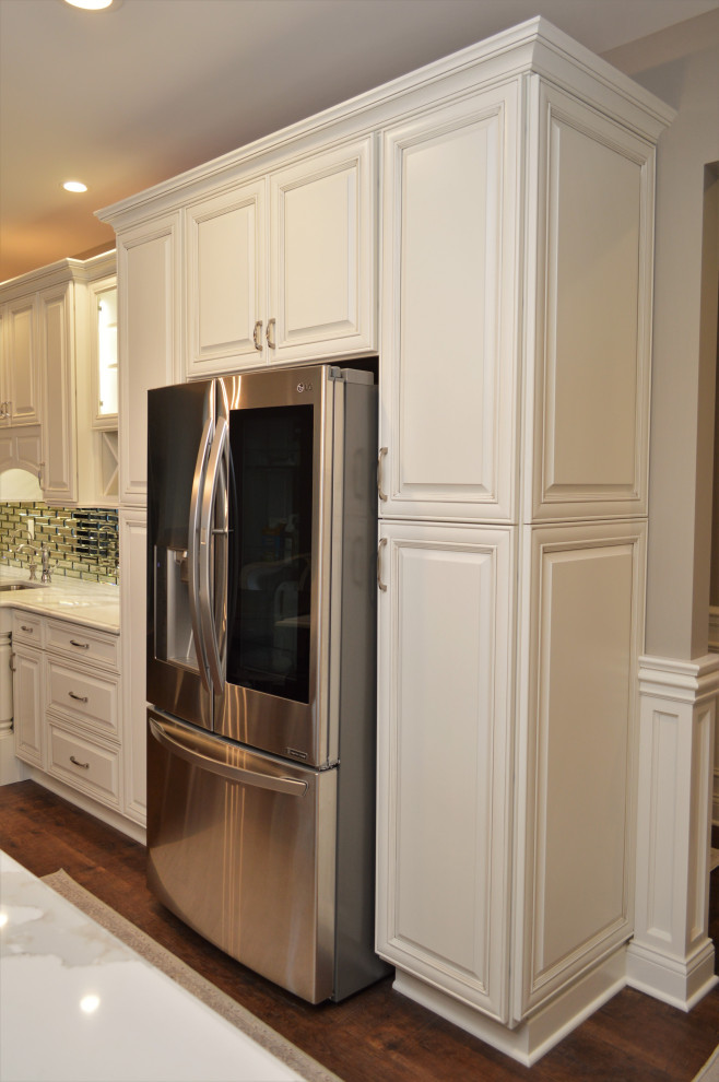Idéer för ett mycket stort klassiskt vit kök, med en undermonterad diskho, luckor med upphöjd panel, vita skåp, bänkskiva i kvartsit, spegel som stänkskydd, rostfria vitvaror, mellanmörkt trägolv, en köksö och brunt golv