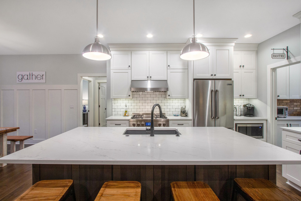 Modern inredning av ett mellanstort vit vitt kök, med en undermonterad diskho, skåp i shakerstil, vita skåp, bänkskiva i kvartsit, vitt stänkskydd, stänkskydd i tunnelbanekakel, rostfria vitvaror, mörkt trägolv, en köksö och brunt golv