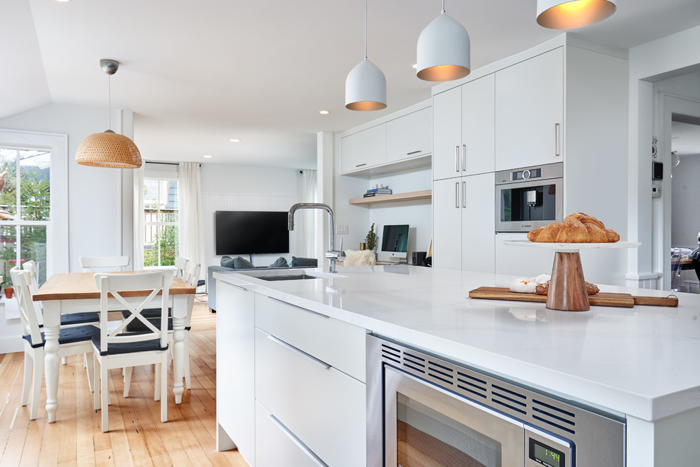 Inspiration for a large modern l-shaped light wood floor and brown floor eat-in kitchen remodel in Vancouver with an undermount sink, flat-panel cabinets, white cabinets, quartz countertops, white backsplash, porcelain backsplash, stainless steel appliances, an island and white countertops