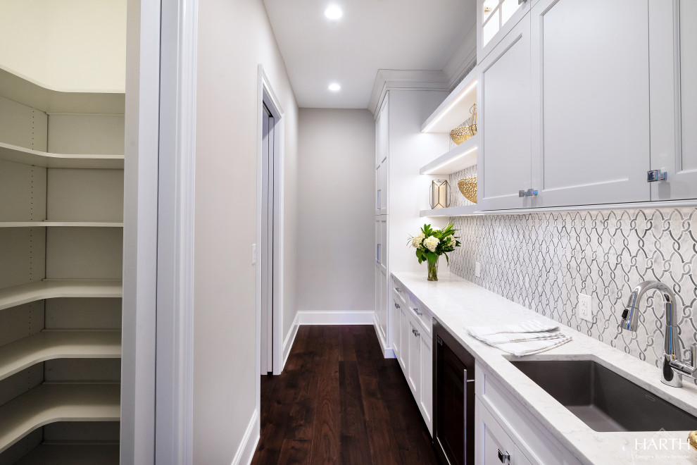 Example of a large transitional single-wall dark wood floor and brown floor kitchen pantry design in Philadelphia with an undermount sink, recessed-panel cabinets, white cabinets, quartz countertops, white backsplash, porcelain backsplash, stainless steel appliances, no island and white countertops
