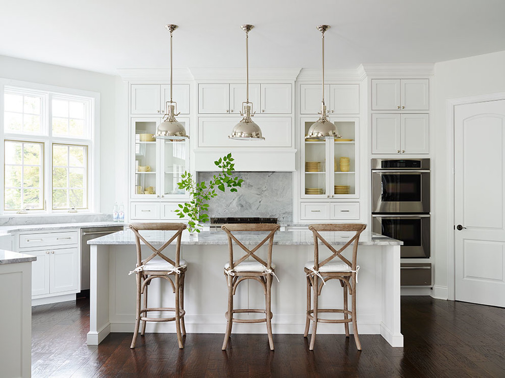 Example of a classic dark wood floor kitchen design in Philadelphia with glass-front cabinets, white cabinets, gray backsplash, stainless steel appliances and an island