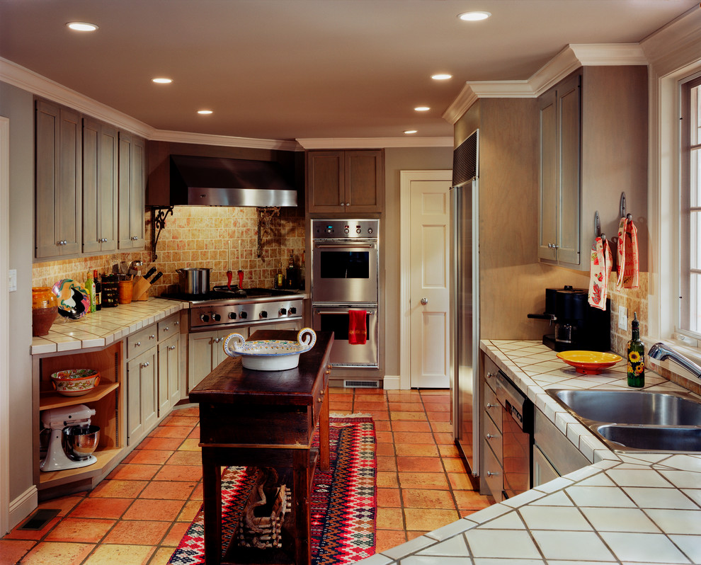 Example of a large transitional galley terra-cotta tile enclosed kitchen design in Philadelphia with a double-bowl sink, shaker cabinets, beige cabinets, tile countertops, brown backsplash, stone tile backsplash, stainless steel appliances and no island
