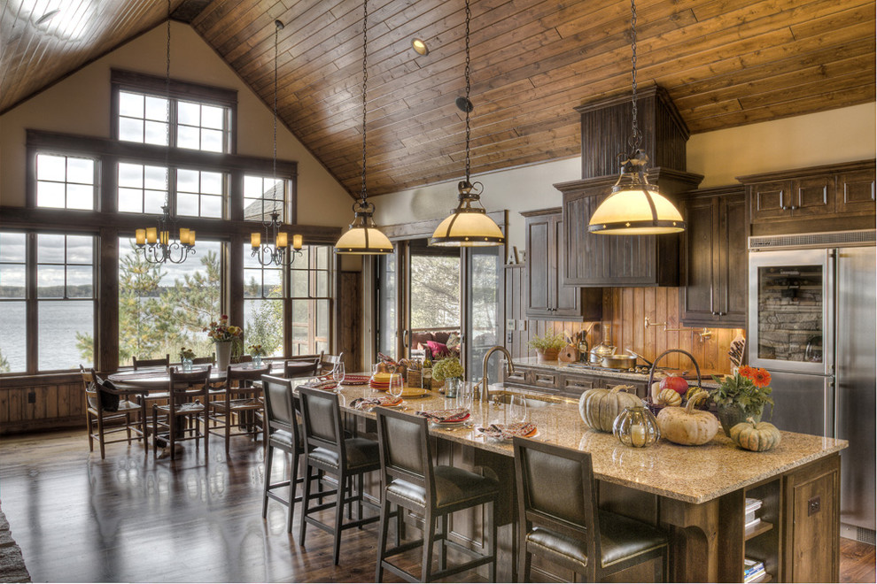 Photo of a large rustic galley kitchen/diner in Minneapolis with a submerged sink, raised-panel cabinets, brown cabinets, granite worktops, brown splashback, wood splashback, stainless steel appliances, dark hardwood flooring, an island and brown floors.