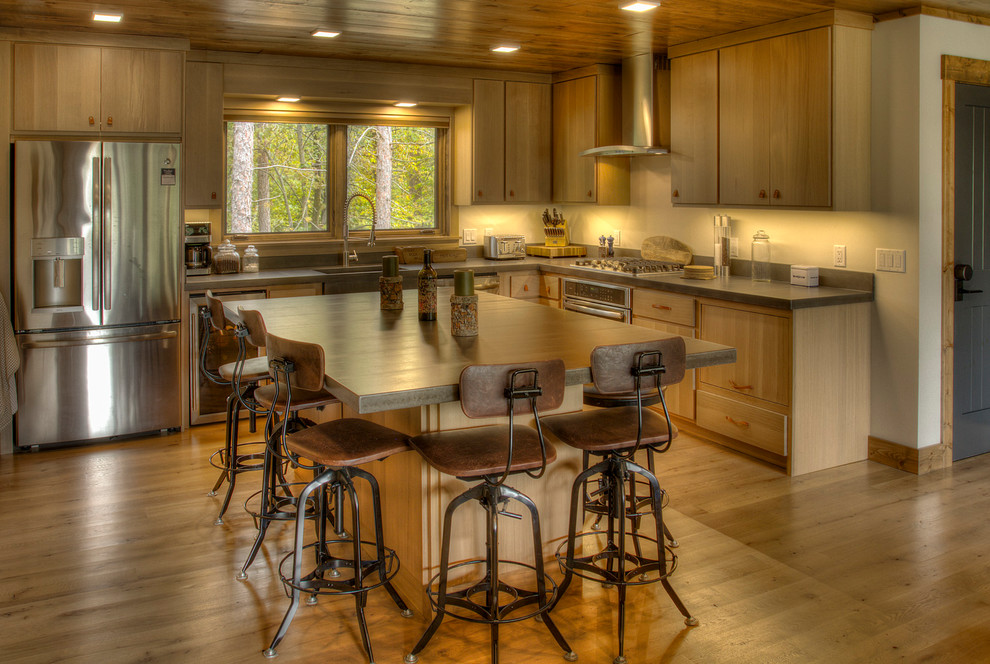 Rustikale Küche in L-Form mit Landhausspüle, flächenbündigen Schrankfronten, hellbraunen Holzschränken, braunem Holzboden, Kücheninsel, braunem Boden und grauer Arbeitsplatte in Minneapolis