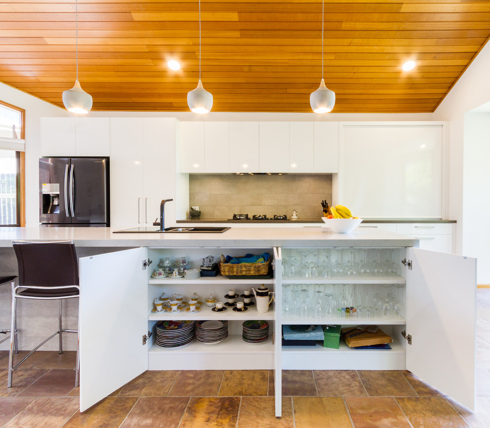 Foto på ett stort funkis grå kök, med en nedsänkt diskho, släta luckor, vita skåp, bänkskiva i kvarts, rostfria vitvaror, klinkergolv i porslin, en köksö, brunt golv och brunt stänkskydd
