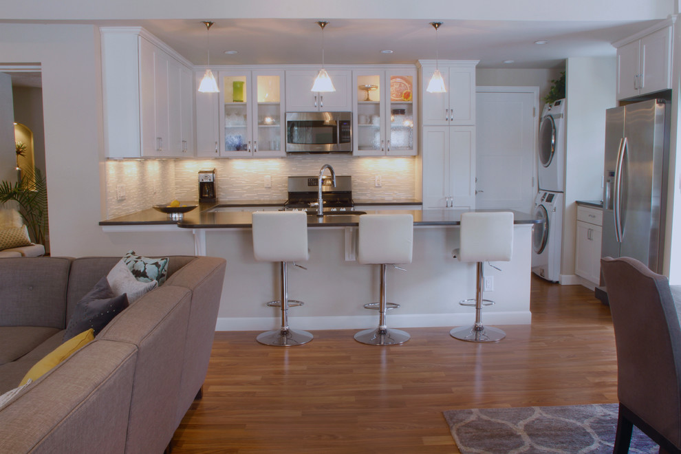 Bild på ett mellanstort funkis kök, med en dubbel diskho, skåp i shakerstil, vita skåp, bänkskiva i kvarts, grått stänkskydd, stänkskydd i glaskakel, rostfria vitvaror, mellanmörkt trägolv och en halv köksö