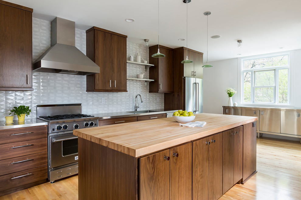 Example of a mid-sized trendy single-wall light wood floor kitchen design in Minneapolis with an integrated sink, flat-panel cabinets, medium tone wood cabinets, stainless steel countertops, white backsplash, porcelain backsplash, stainless steel appliances and an island