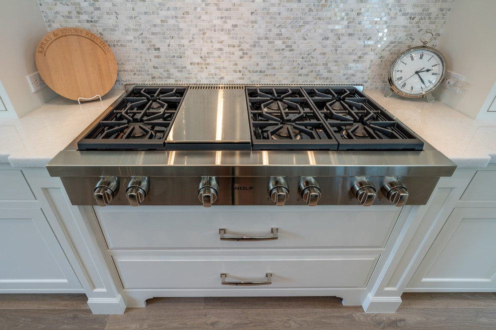 Esempio di una cucina stile marinaro di medie dimensioni con ante a filo, ante bianche, top in marmo, elettrodomestici da incasso, parquet chiaro, pavimento marrone e top bianco