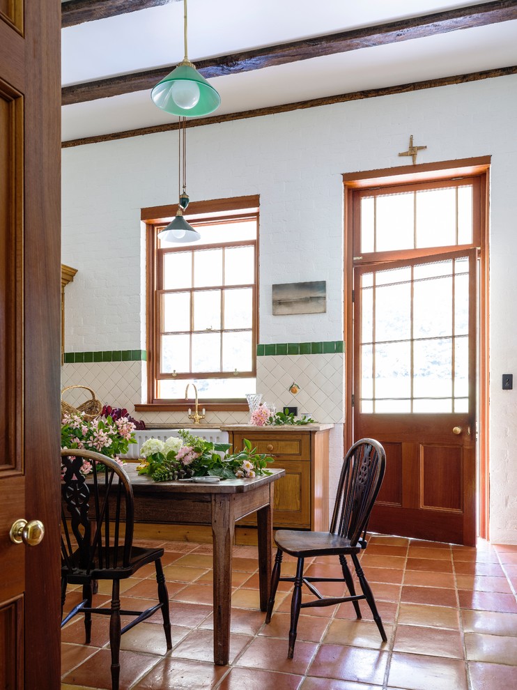 Foto på ett lantligt kök, med en rustik diskho, luckor med infälld panel, skåp i ljust trä, marmorbänkskiva, vitt stänkskydd, stänkskydd i keramik, klinkergolv i terrakotta och svarta vitvaror