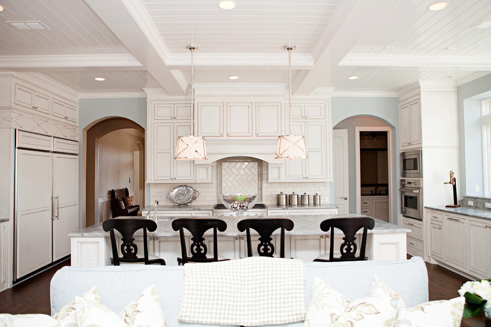 Exempel på ett stort klassiskt grå grått kök, med integrerade vitvaror, vita skåp, vitt stänkskydd, stänkskydd i tunnelbanekakel, en undermonterad diskho, luckor med infälld panel, marmorbänkskiva, mörkt trägolv, en köksö och brunt golv