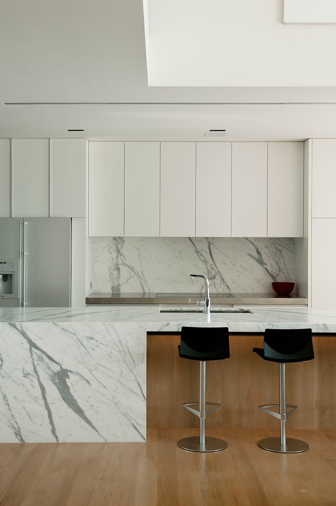 Exempel på ett modernt kök, med vitt stänkskydd, stänkskydd i sten, rostfria vitvaror, släta luckor, en undermonterad diskho och marmorbänkskiva