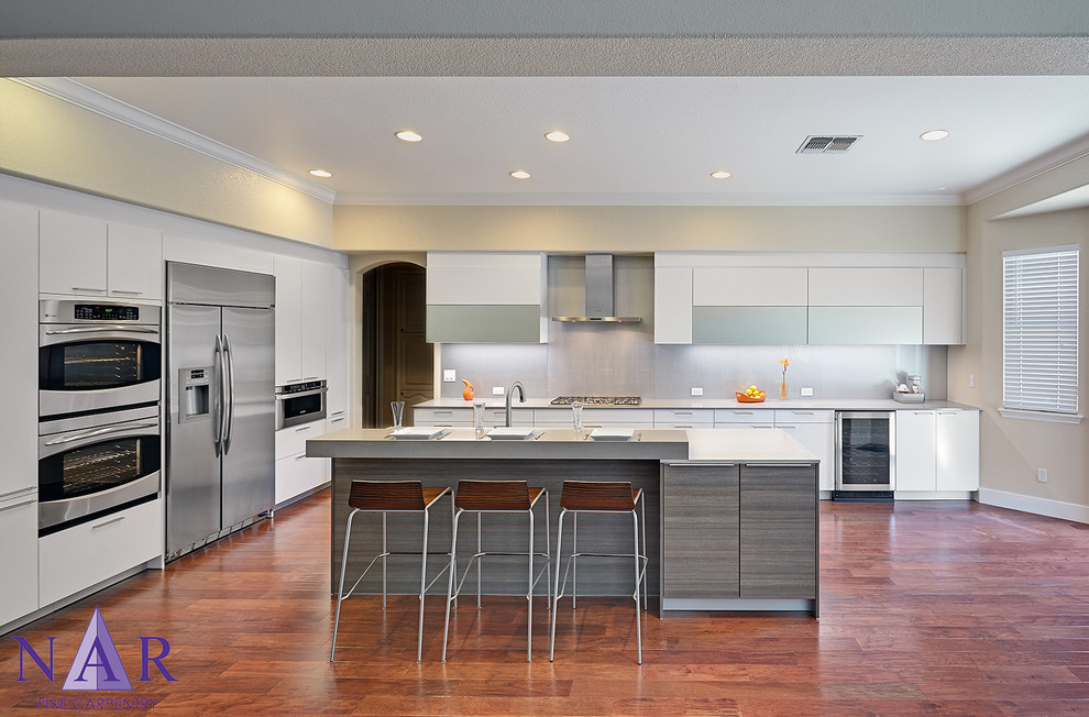 Design ideas for a medium sized contemporary l-shaped open plan kitchen in Sacramento with a single-bowl sink, flat-panel cabinets, white cabinets, engineered stone countertops, grey splashback, glass sheet splashback, stainless steel appliances, medium hardwood flooring and an island.