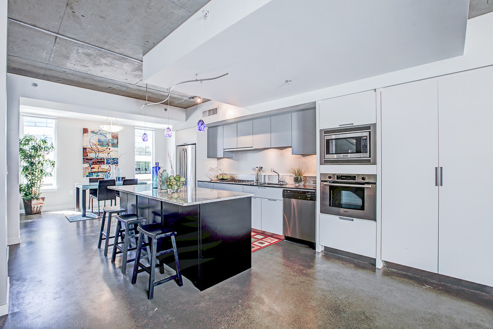 Example of a large urban single-wall concrete floor eat-in kitchen design in Seattle with flat-panel cabinets, light wood cabinets, granite countertops, stainless steel appliances and an island