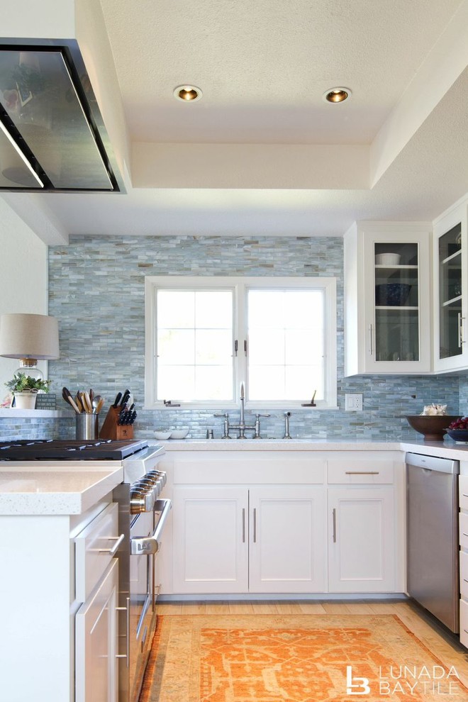 Foto på ett mellanstort vintage kök, med en undermonterad diskho, luckor med glaspanel, vita skåp, bänkskiva i kvarts, blått stänkskydd, stänkskydd i stickkakel, rostfria vitvaror, ljust trägolv och en halv köksö