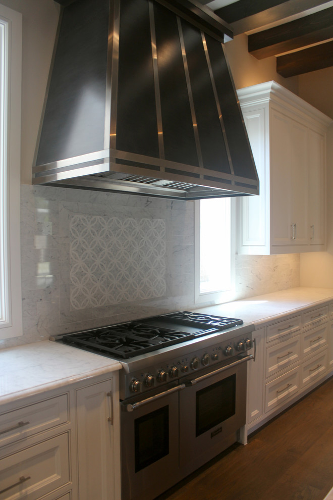 Inredning av ett klassiskt kök, med luckor med infälld panel, vita skåp, vitt stänkskydd, stänkskydd i marmor, rostfria vitvaror, mellanmörkt trägolv och brunt golv