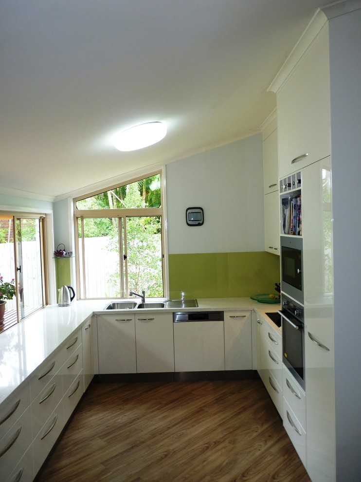Idéer för att renovera ett mellanstort funkis u-kök, med en nedsänkt diskho, släta luckor, vita skåp, bänkskiva i kvarts, grönt stänkskydd, glaspanel som stänkskydd och rostfria vitvaror