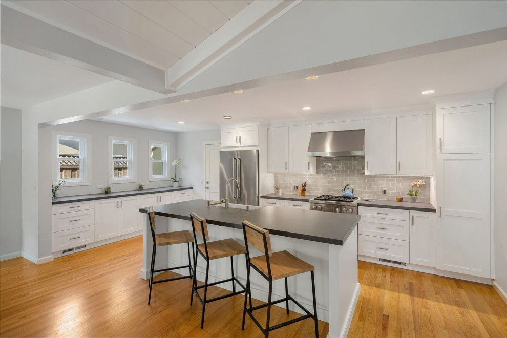 Klassisk inredning av ett stort grå grått kök, med en rustik diskho, skåp i shakerstil, vita skåp, bänkskiva i kvarts, beige stänkskydd, stänkskydd i glaskakel, rostfria vitvaror, mellanmörkt trägolv, en köksö och brunt golv