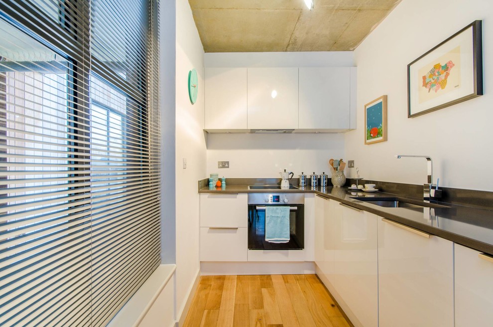 Offene, Kleine Moderne Küche ohne Insel in L-Form mit integriertem Waschbecken, Glasfronten, weißen Schränken, Quarzwerkstein-Arbeitsplatte, Küchengeräten aus Edelstahl und braunem Holzboden in London