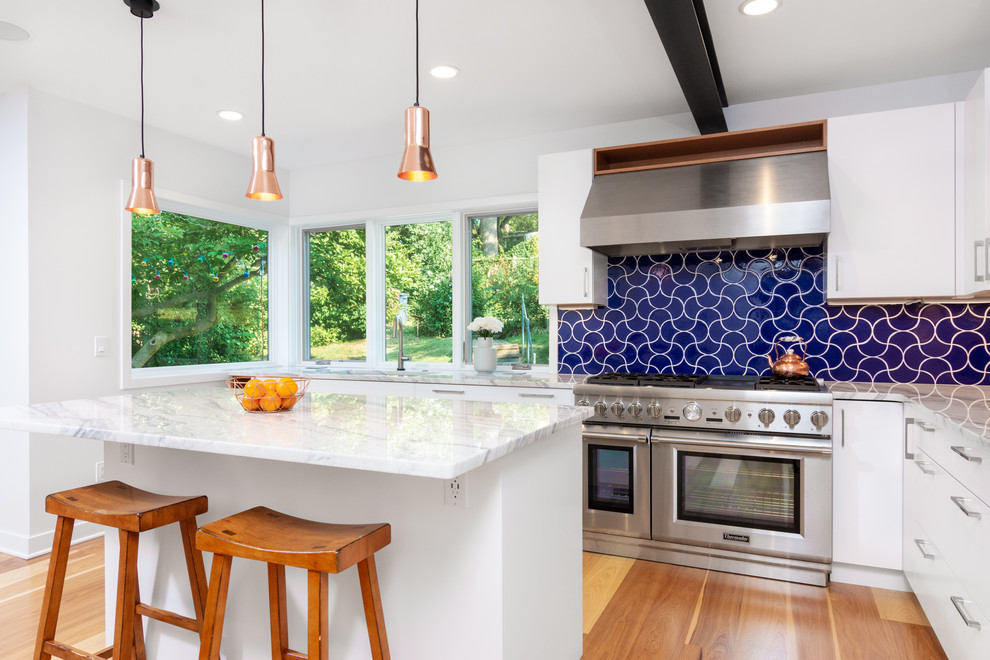 Example of a country l-shaped light wood floor kitchen design in Detroit with an undermount sink, flat-panel cabinets, white cabinets, marble countertops, blue backsplash, stainless steel appliances, an island, white countertops and cement tile backsplash