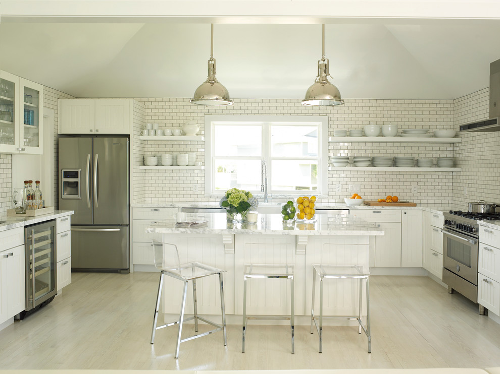 Large beach style u-shaped open plan kitchen in Houston with a belfast sink, open cabinets, white cabinets, marble worktops, white splashback, metro tiled splashback, stainless steel appliances, light hardwood flooring and an island.