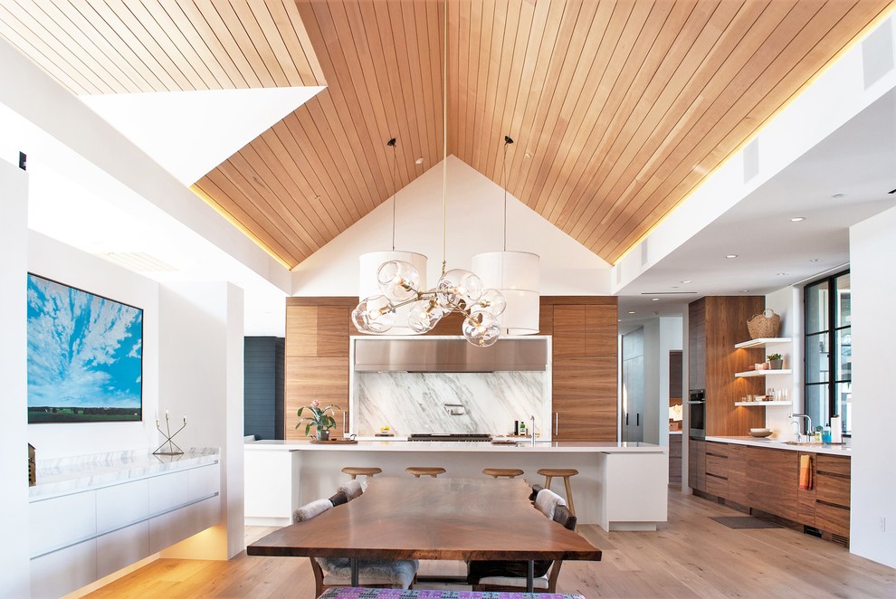 Moderne Wohnküche mit flächenbündigen Schrankfronten, hellbraunen Holzschränken, Küchenrückwand in Weiß, hellem Holzboden und Kücheninsel in Denver