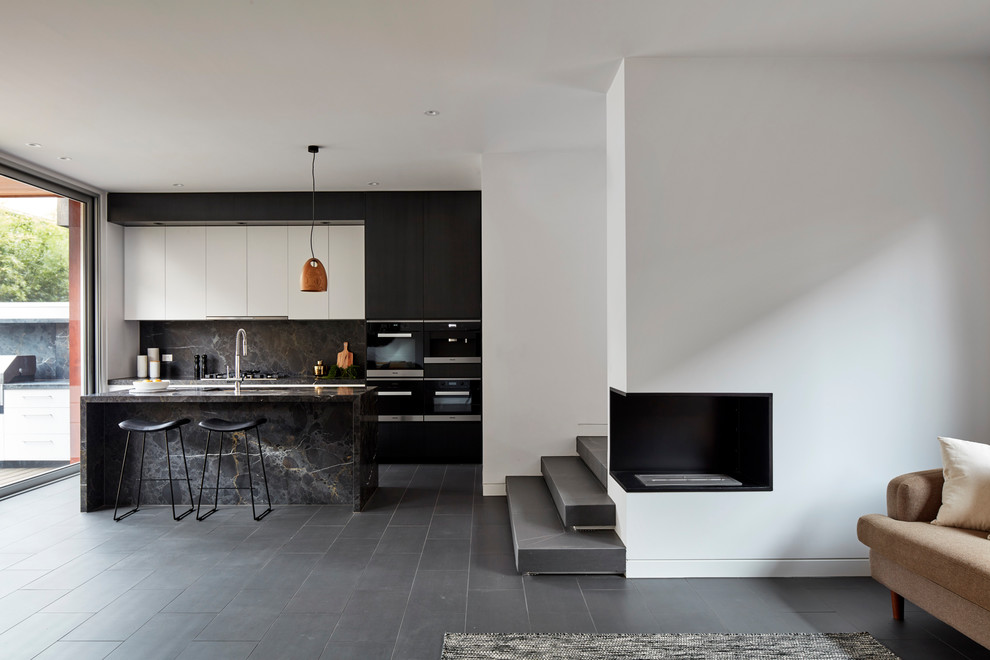 Modern inredning av ett mellanstort svart svart kök med öppen planlösning, med en undermonterad diskho, släta luckor, svarta skåp, marmorbänkskiva, svart stänkskydd, stänkskydd i sten, svarta vitvaror, klinkergolv i porslin, en köksö och grått golv