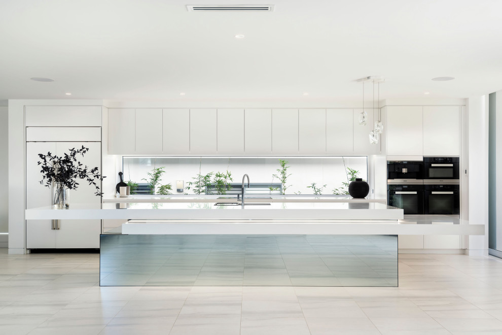 Expansive contemporary galley kitchen in Other with white cabinets, engineered stone countertops, black appliances, an island and white worktops.