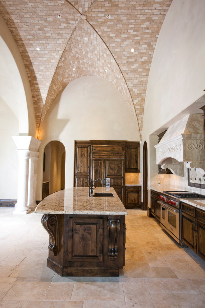 Ejemplo de cocinas en L mediterránea, extra grande, abierta, con fregadero encastrado, armarios con paneles con relieve, puertas de armario de madera en tonos medios, encimera de mármol, salpicadero beige, salpicadero de azulejos de piedra, electrodomésticos de acero inoxidable, suelo de travertino y una isla