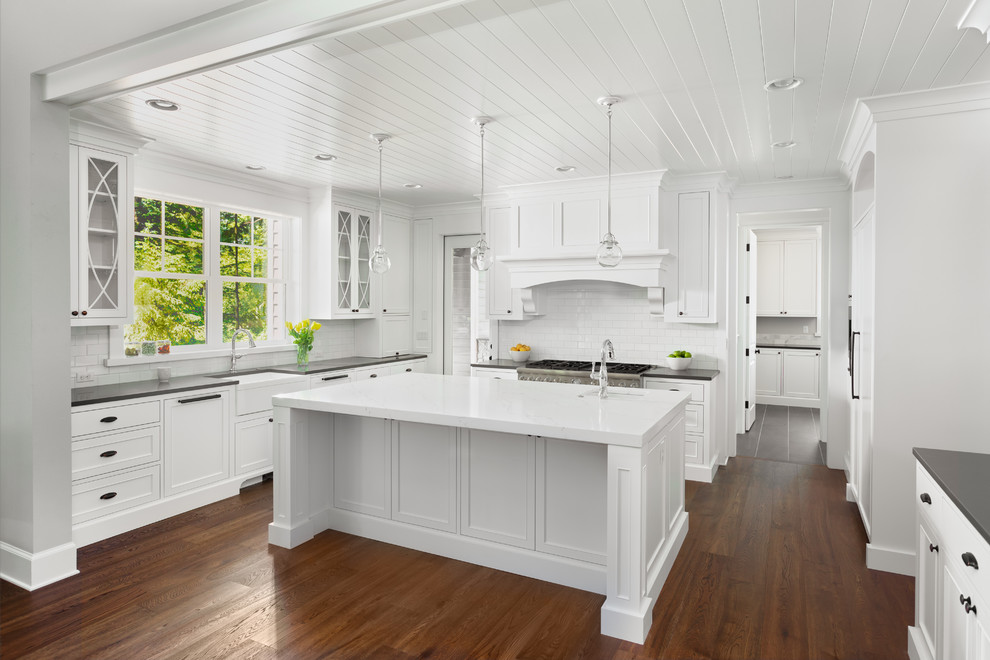 Example of a large transitional galley medium tone wood floor and brown floor eat-in kitchen design in Seattle with a farmhouse sink, recessed-panel cabinets, white cabinets, quartzite countertops, white backsplash, ceramic backsplash, stainless steel appliances, an island and gray countertops