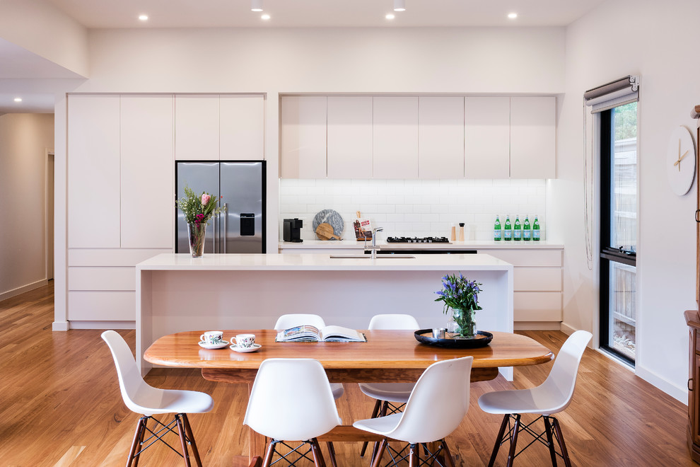 Inspiration for a mid-sized contemporary galley medium tone wood floor eat-in kitchen remodel in Melbourne with an undermount sink, flat-panel cabinets, white cabinets, white backsplash, ceramic backsplash, stainless steel appliances and an island